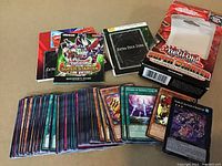Photo of a large collection of Yu-Gi-Oh! cards in sleeves, two official game guide booklets, an Extra Deck Zone playmat, and the original product box.
