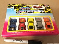 Photo of a sealed blister pack containing five new diecast metal cars labeled 'New Motorsport'. Cars are various colors and designs. A Sharpie pen shown for size reference.