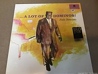 Front cover of sealed Fats Domino vinyl LP titled "...A Lot of Dominos!" featuring yellow and brown artwork with Fats Domino illustration and 180 gram sticker.