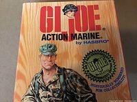 Front of box showing G.I. Joe Action Marine by Hasbro logo, 16th Anniversary stamp with collectible number 85468, wood grain style background.