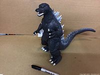 Full body view of the black Godzilla figure standing against a cardboard background with a Sharpie for scale.