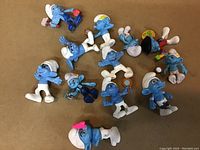 Top view of 12 Smurf plastic figurines arranged on a flat surface showing various poses and colors.