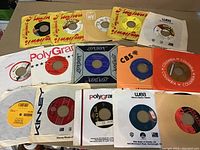 Fifteen 45 RPM vinyl records arranged showing different label designs and sleeves from multiple brands.