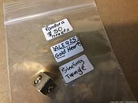 Clear close-up of Pandora charm in a zip-lock bag with labels describing it as Pandora 925 with gold hearts and a sterling silver triangle.