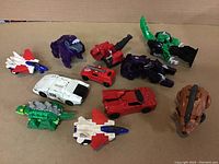 Top-down photo of 11 various Transformers figures and vehicles on a carpeted surface.