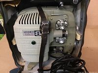 Close-up inside view of vintage Sekonic 8mm film projector, showing lens, controls, and attached power cord.