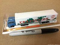 Blue and white Transfrigo diecast truck sealed in plastic packaging with cardboard backing, placed beside a Sharpie marker for size comparison.