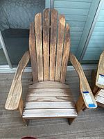 Front view of the wooden Adirondack chair showing the weathered wooden slats, seat, and wide armrests.