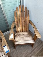 Full view of weathered wooden Adirondack chair with wide armrests and slatted seat and backrest on balcony floor near window.