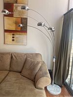 Full view of the arc floor lamp positioned beside a sofa, showing five chrome metal arms with hanging lamps and curved design.