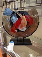 Full view of art glass sculpture on black metal base, showing color and shape details.