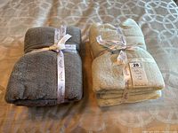 Two bundled sets of bath towels on bed. One set grey, the other mint green, tied with branded white ribbons.