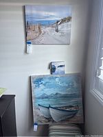 Three beach-themed wall art pieces: two canvas photo prints and one smaller painting on wood, arranged on a white wall near a window.