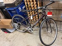 Photo showing full left side view of the bicycle with drop handlebars, black saddle, and road tires on silver rims against a storage background.