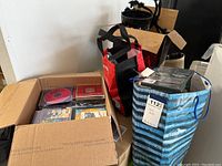 Photo showing several boxes and bags filled with various CDs and DVDs in jewel cases and paper sleeves.