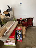 General view of Christmas decoration items stored in bins and boxes including wrapped rolls, boxed artificial tree, and fabric decor.