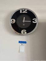 Front view of Cupecoy wall clock showing black face with large white numerals and silver frame.