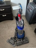 Front view of Dyson DC24 vacuum with dust bin and attached cleaning head, showing clear container and blue motor housing.