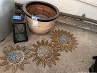 Photo showing the three wooden sunburst wall arts, the large earthenware plant pot, and the metal lantern candleholder arranged on a concrete floor.
