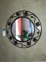 Full view of the round wall mirror hanging on a textured wall, showing the wrought iron frame with leaf and grapevine details.