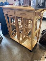Side view of wooden kitchen island on rollers showing two inset drawers above and a shelf below with two wooden stools nested underneath.