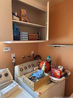 Laundry area with washing machine, dryer, shelf with detergent, baking soda, iron, and cleaning supplies.