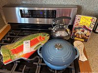 Overview of all items including Le Creuset pot, fish potholders, stove kettle, cookbook, and stand