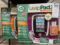 Photo showing two unopened LeapFrog LeapPad2 Power learning tablets in their original packaging with detailed front box views including included rechargeable packs and educational features.