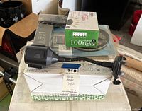 Stack of items including black phone holder designed for car cup holders, box of 100 ultra-bright white mini lights, solar-powered white candy lantern, and packaging box below.