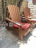 Angled front view of brown Lifetime Adirondack chair with red cushion on stone patio, displaying chair's design and cushion.