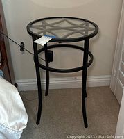 Side view of the small round table showing black metal base and clear glass top in corner of room.