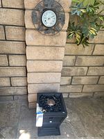 Outdoor heater with black square base and faux lava rocks on top.
