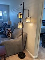 Photo showing full height metal floor lamp with three pendant lights over sofa and carpeted floor