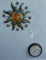 Both metal sun wall art with glass face and La Crosse barometer hanging side by side on exterior wall, showing full items and measurements.