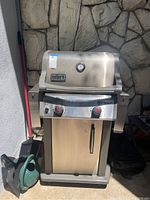 Front view of the Weber Spirit 2 gas barbecue grill showing the stainless steel hood, two control knobs with red accents, and lower cabinet door with handle.