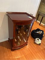 Front diagonal view of wooden wine cabinet with removable top tray and glass front door, showing wine bottle storage inside.