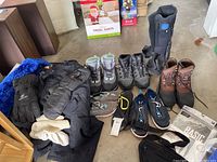 Photo of winter boots, gloves, and pants arranged on floor with Santa decoration in background.