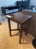 Wooden end table positioned next to a couch, showing the top and leg structure with visible scratches.