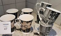Eight ceramic mugs on counter, four with floral design, four with vintage photo design
