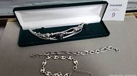 Two costume jewelry bracelets laid out; one multi-stranded with beads and central decorative stone in a velvet-lined box, the other a linked metal chain bracelet.