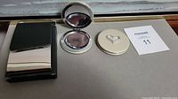 Two round silver plated compacts with heart shape on top and a sleek silver plated business card holder case shown closed.