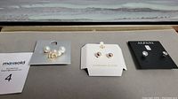 Four pairs of earrings on their original branded display cards including Cezanne, Sterling Silver, and Alfani brands. Display cards show clear brand logos and the earrings include various stud styles such as faux pearls and clear crystals.