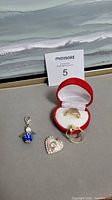 Photo showing all items in the lot including the Guess pendant charm, blue crystal charm, and assorted rings inside and outside a red velvet heart-shaped jewelry box.