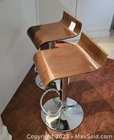 Two adjustable height counter stools placed side by side showing curved wood veneer seats and chrome bases