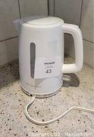 White Toastmaster electric kettle with handle and power cord visible on countertop.
