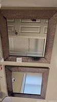 Photo of two square mirrors stacked vertically, showing textured wide frames with damage and reflection of door.