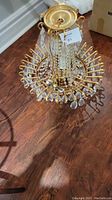 Crystal chandelier viewed from above on wood floor, gold-tone metal frame and hanging clear crystal drops visible.