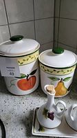 Three ceramic canisters with hand painted fruit designs and lids shown on countertop.