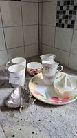 Overview of cups, plates, citrus juicer and decorative leaf-shaped plate on countertop.
