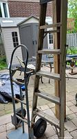 Photo showing the five step aluminum ladder next to the two wheel dolly on a patio area with outdoor furniture and shed in background.